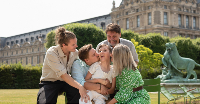 Lucy surrounded by her family outside the Louvre in Paris. One of her brothers is kissing her cheek.
